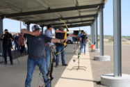 A row of people practice at an archery range.