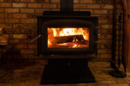 A lit wood stove over a brick background.