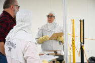 Three individuals in a lab, two wearing protective suits.