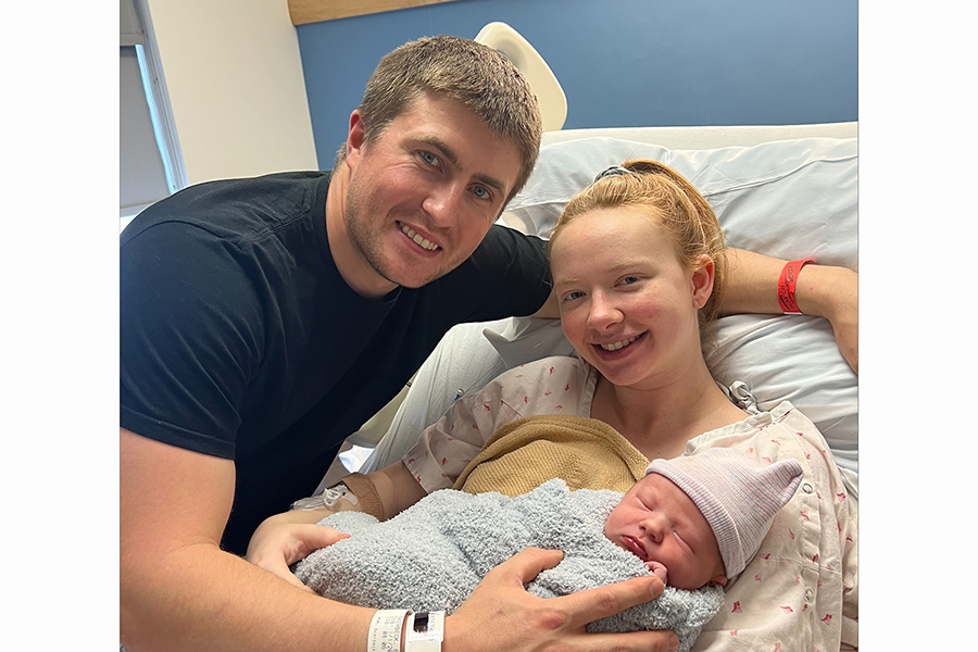 A mother holding a newborn baby in a hospital bed with the father leaning over.